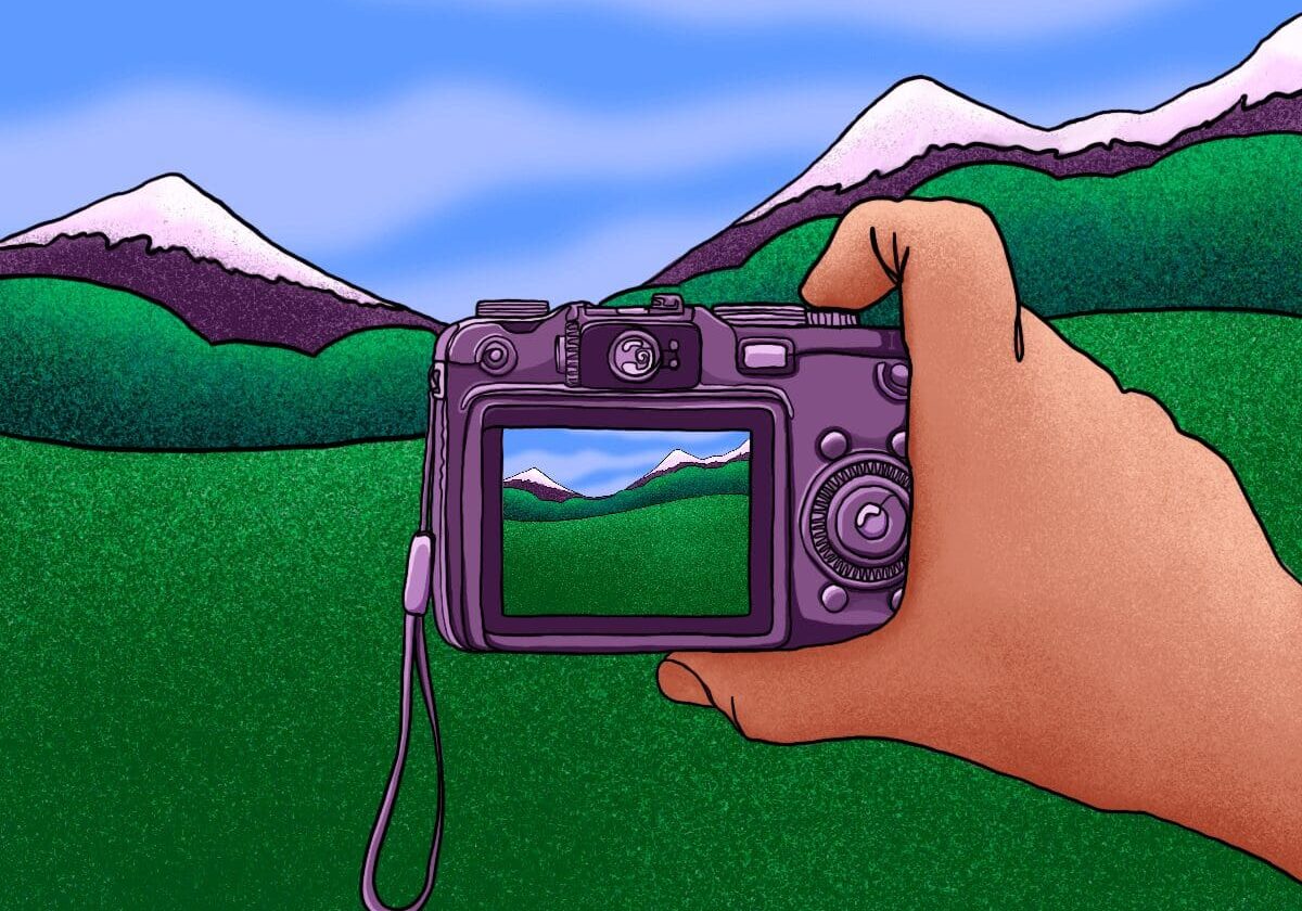 Hand holding camera capturing snowy mountains.